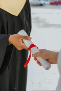 Hands exchanging a graduation diploma wrapped with red ribbon, symbolizing achievement.