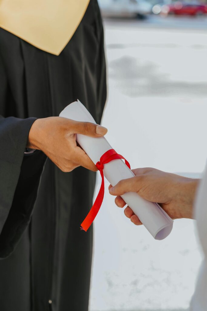 Hands exchanging a graduation diploma wrapped with red ribbon, symbolizing achievement.
